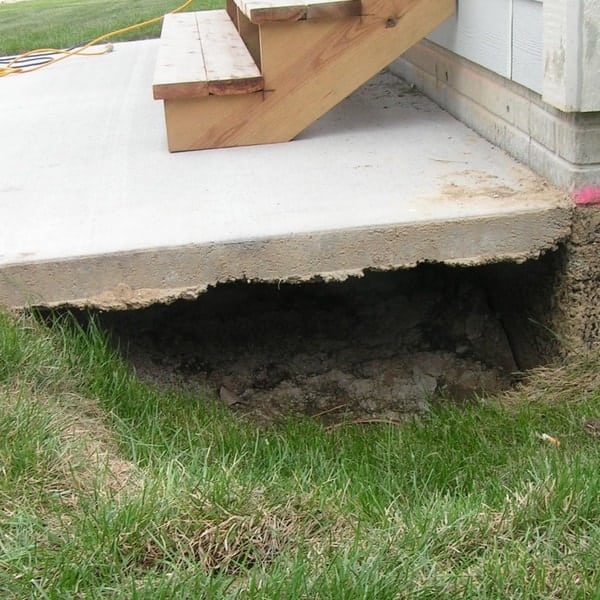 Concrete patio step before void filling, showing a large void and undermined area beneath the concrete slab.